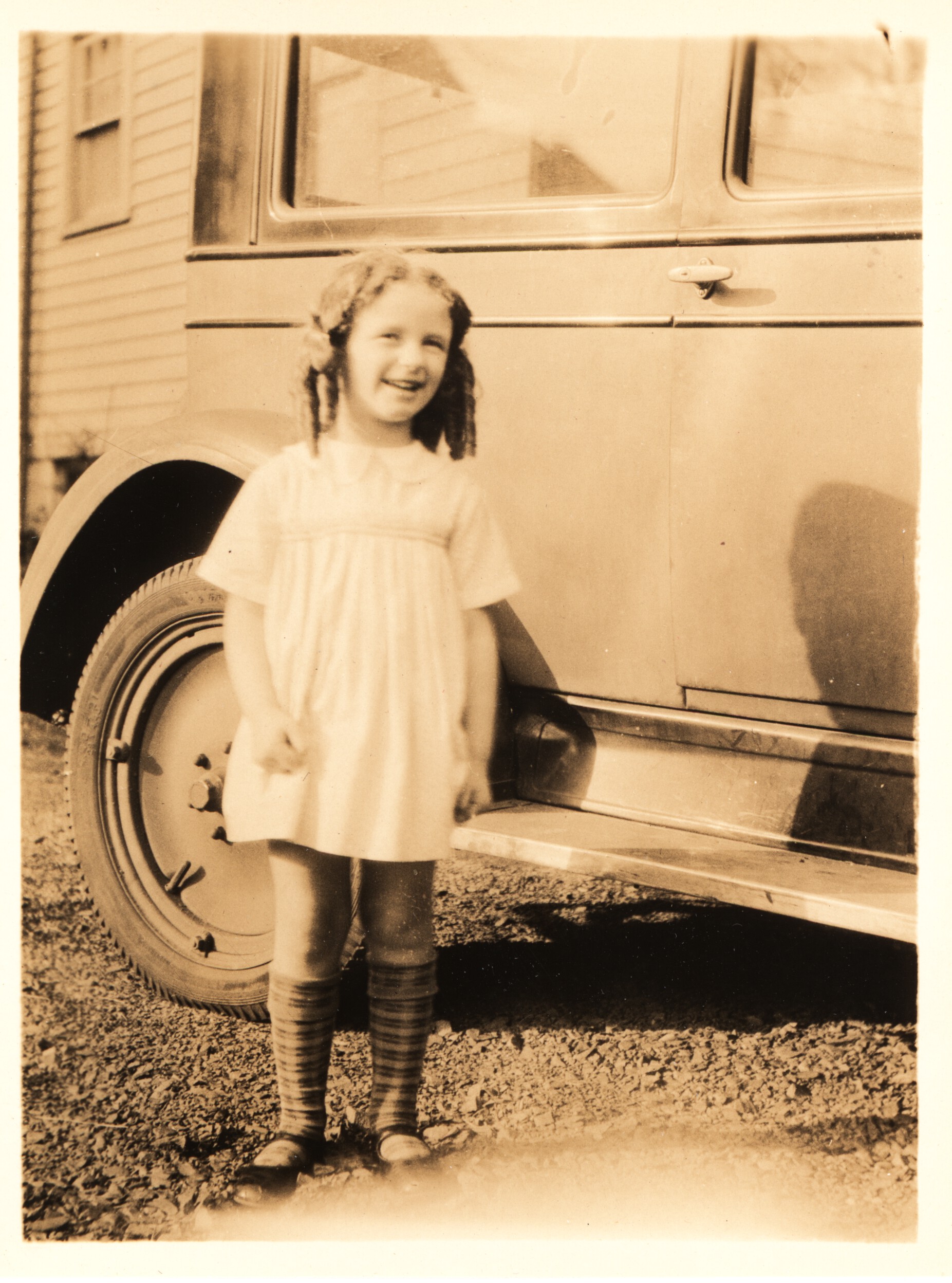 A young girl standing next to a car in the late 1920's/early 1930's