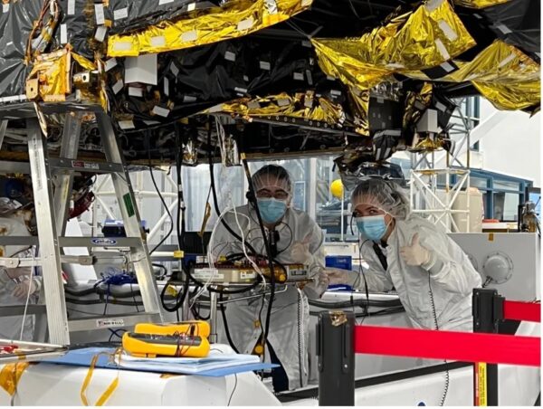 Workers stand under the Psyche spacecraft