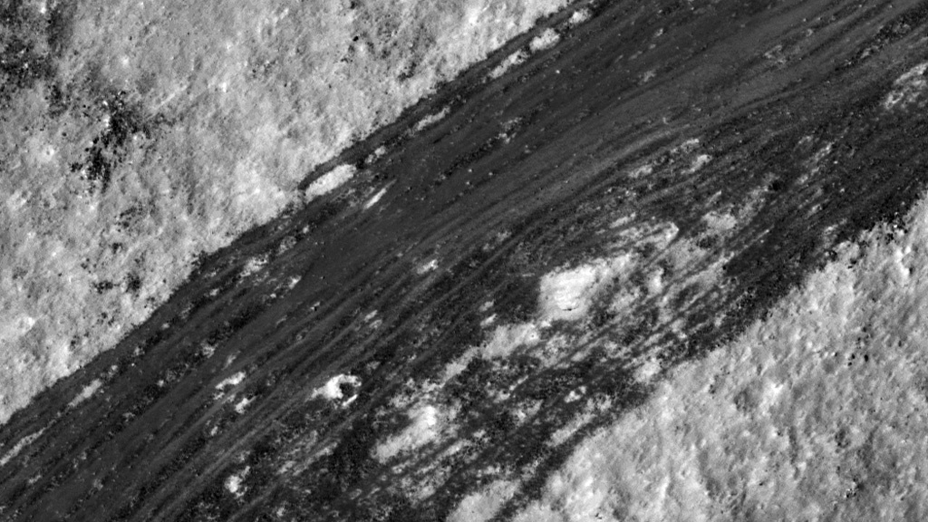 Dark streaks slash from lower left to upper right across the Moon's light grey surface. 