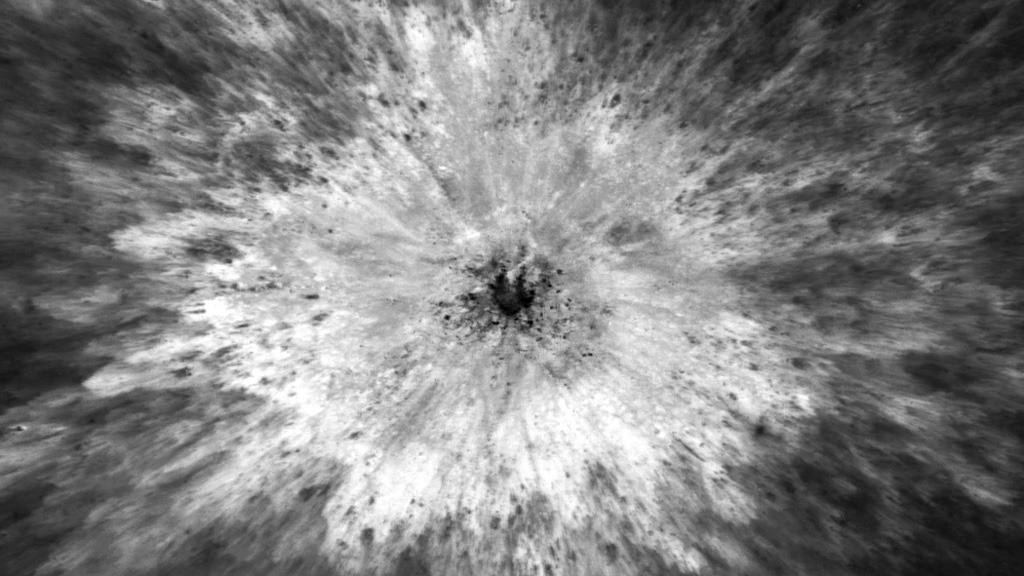 Impact crater with light-colored debris branching out from a dark center. 