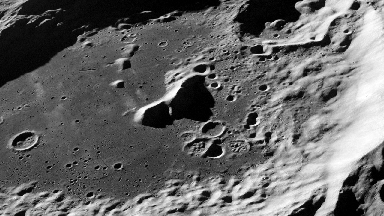 Oblique overhead view of lunar surface, with a bright, peaked ridge filling the right edge of the image. Towards the center and left, the grey surface is marked by craters, and steep hills cast dark shadows.