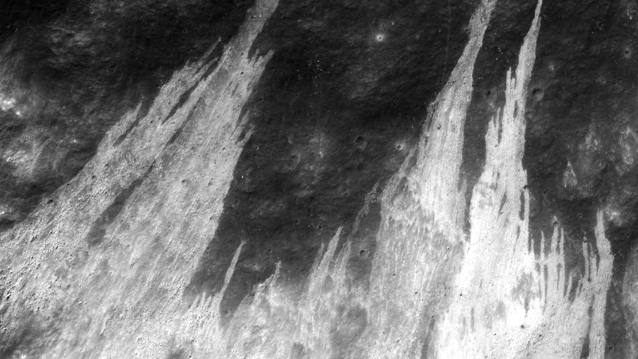 Light-colored streaks of debris on the dark grey lunar surface. 