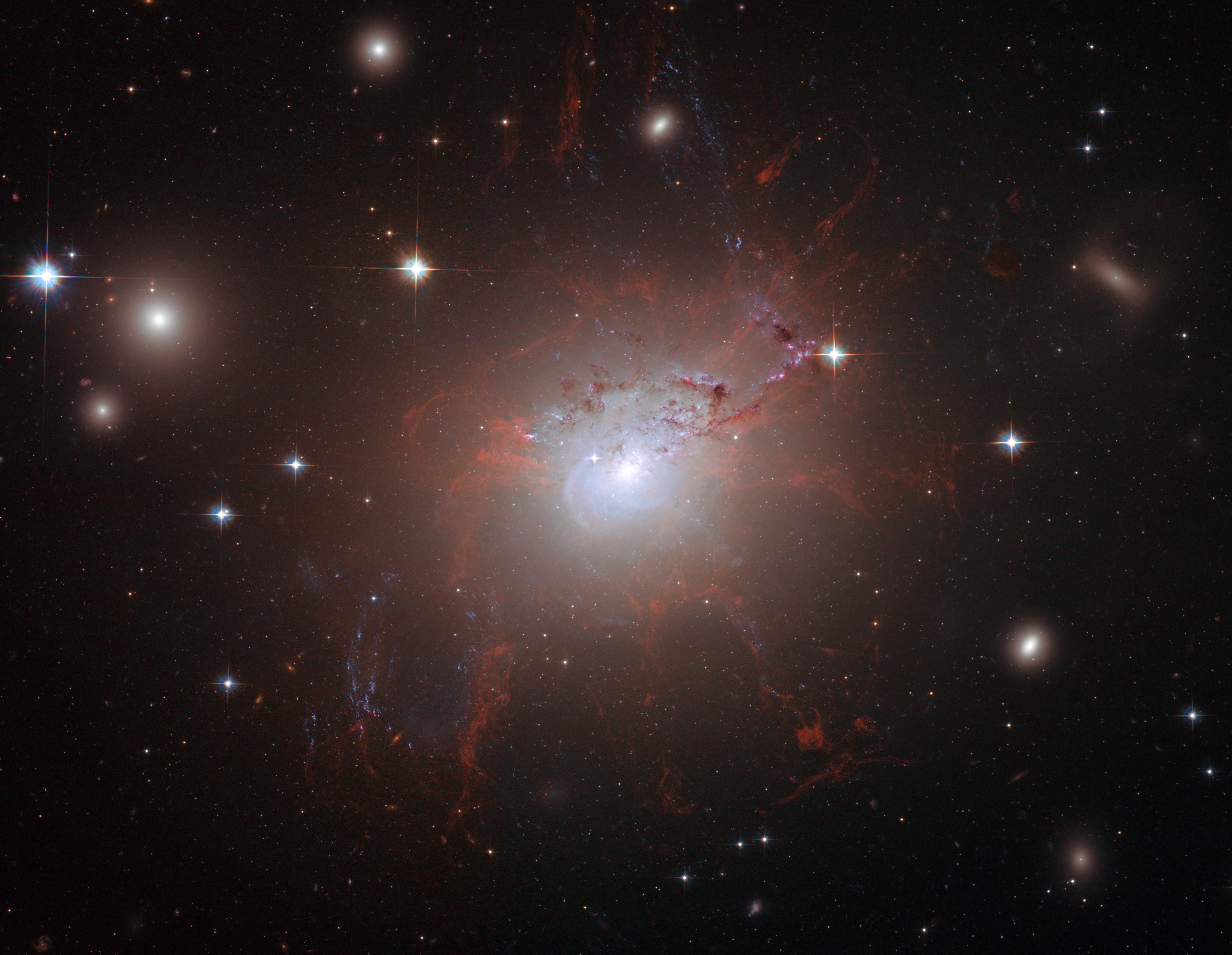 A galaxy with red filaments of gas protruding from it in multiple directions.