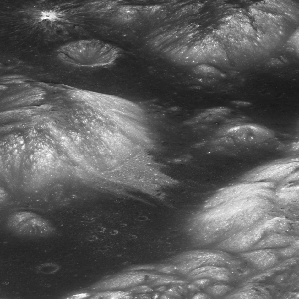 lunar surface with craters and hills. Hillsides are streaked with light grey and white. 