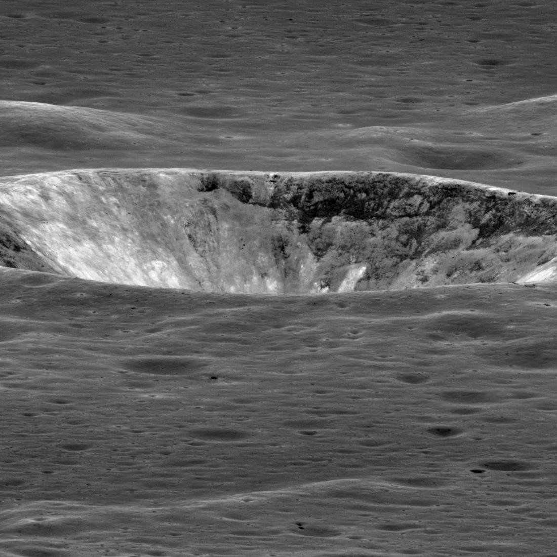Crater with light and dark grey patches, seen almost edge-on from a low oblique angle.