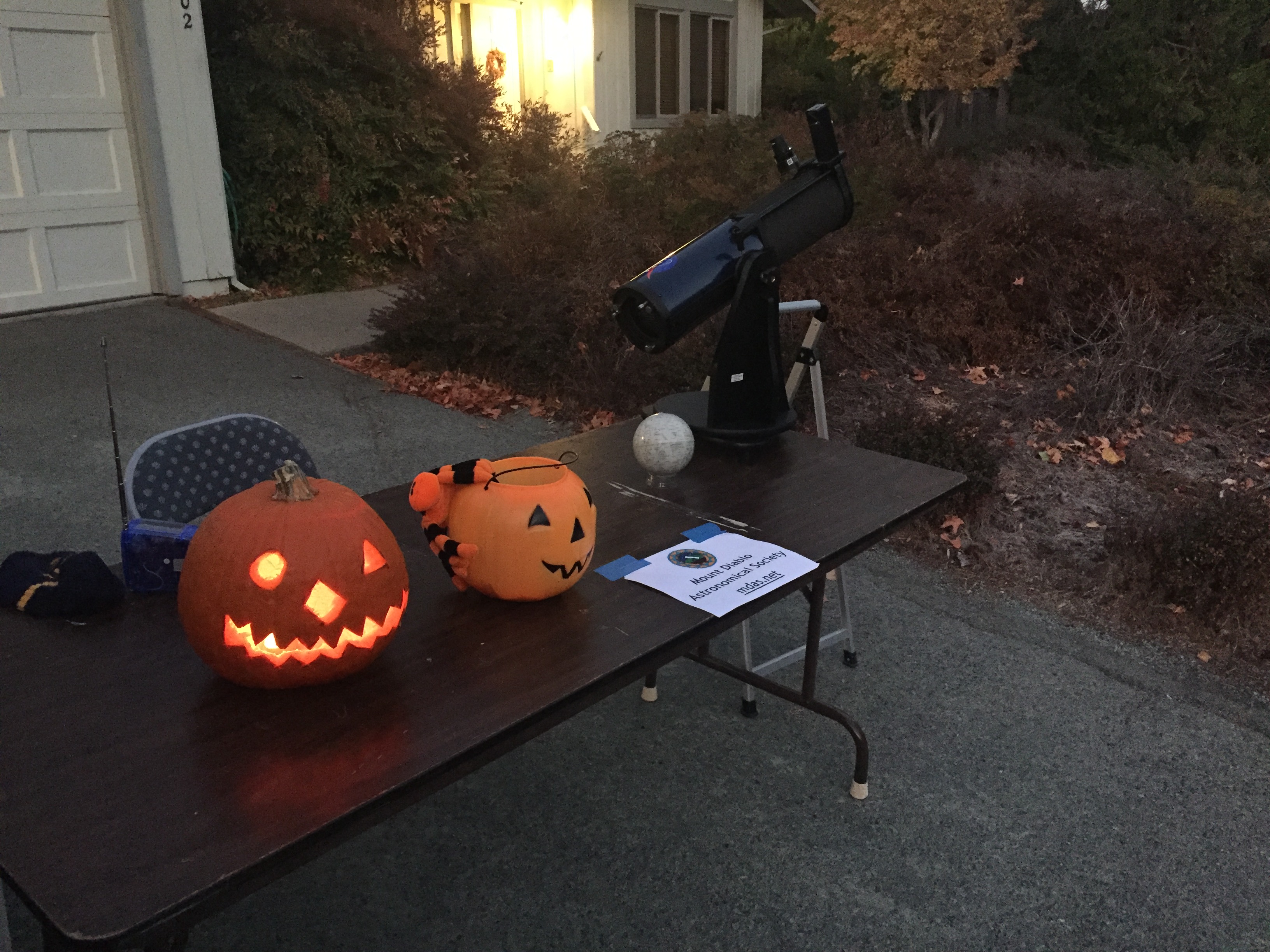 A black telescope set up on a brown table, next to two orange pumpkins