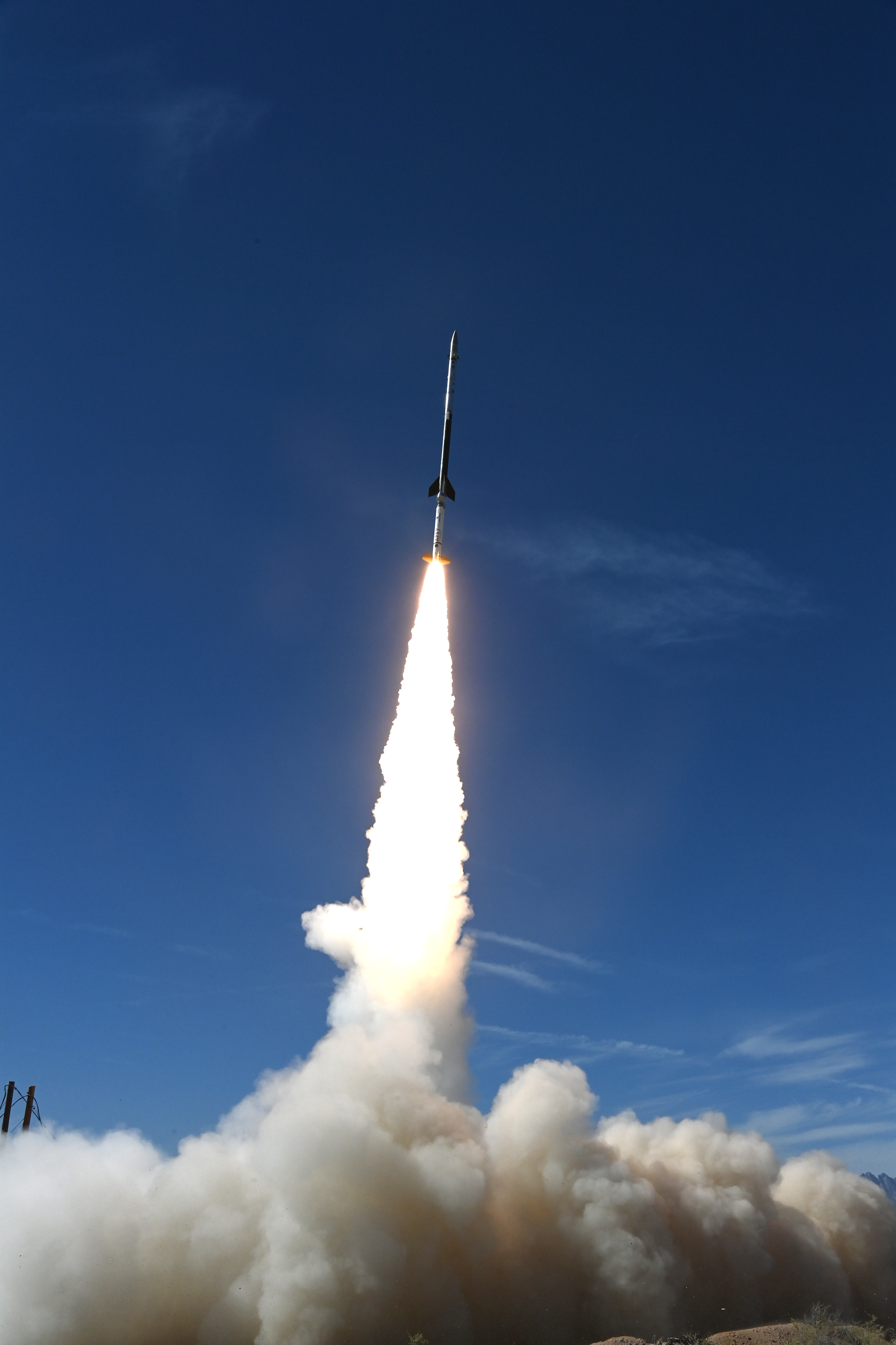 A rocket launches against a blue sky. A cloud of dust gathers below the rocket.
