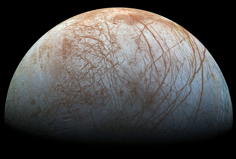 Half of Europa is visible. It is a dark, cream-colored world with reddish-brown streaks/cracks in its icy surface.