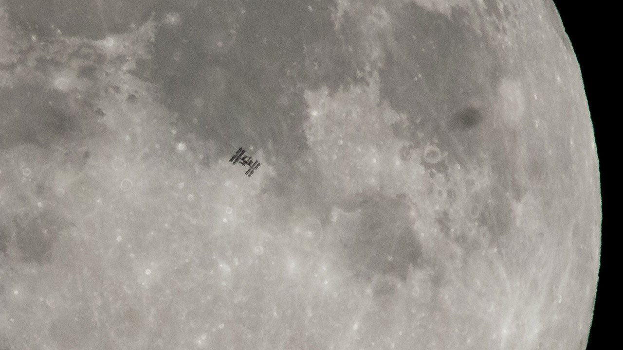 Space station seen in dark outline in front of the Moon.