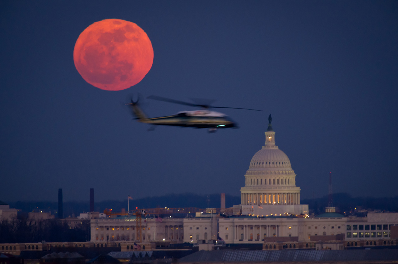 Helicopter flying past full moon and U.S. Capitol.