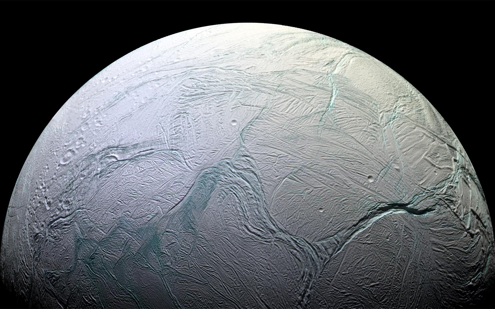 A half circle, with turquoise cracks across the left side its pale blue surface. Craters are shown along its middle and lower right sides.