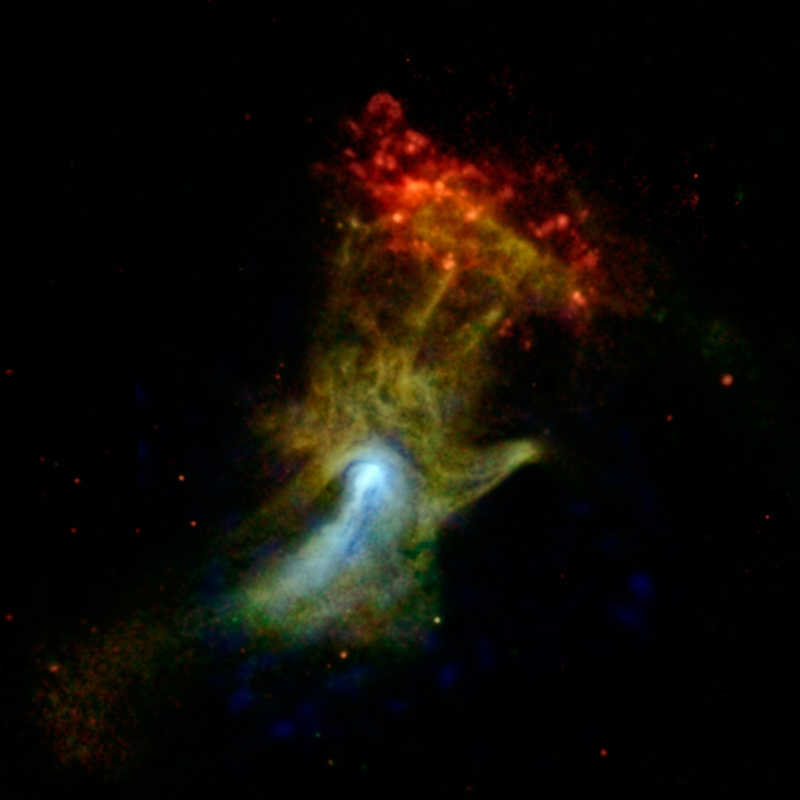 A supernova remnant rises like an ethereal hand up the center of the image. The “wrist” appears in bright white while the finger-like structures are formed from a tangle of yellow strands of emission. This hand-shaped nebula intersects a spotty red oval with dots of light.