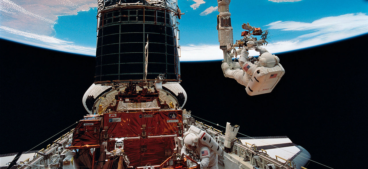 An astronaut is seen at the end of a robotic arm to repair the Hubble Space Telescope.
