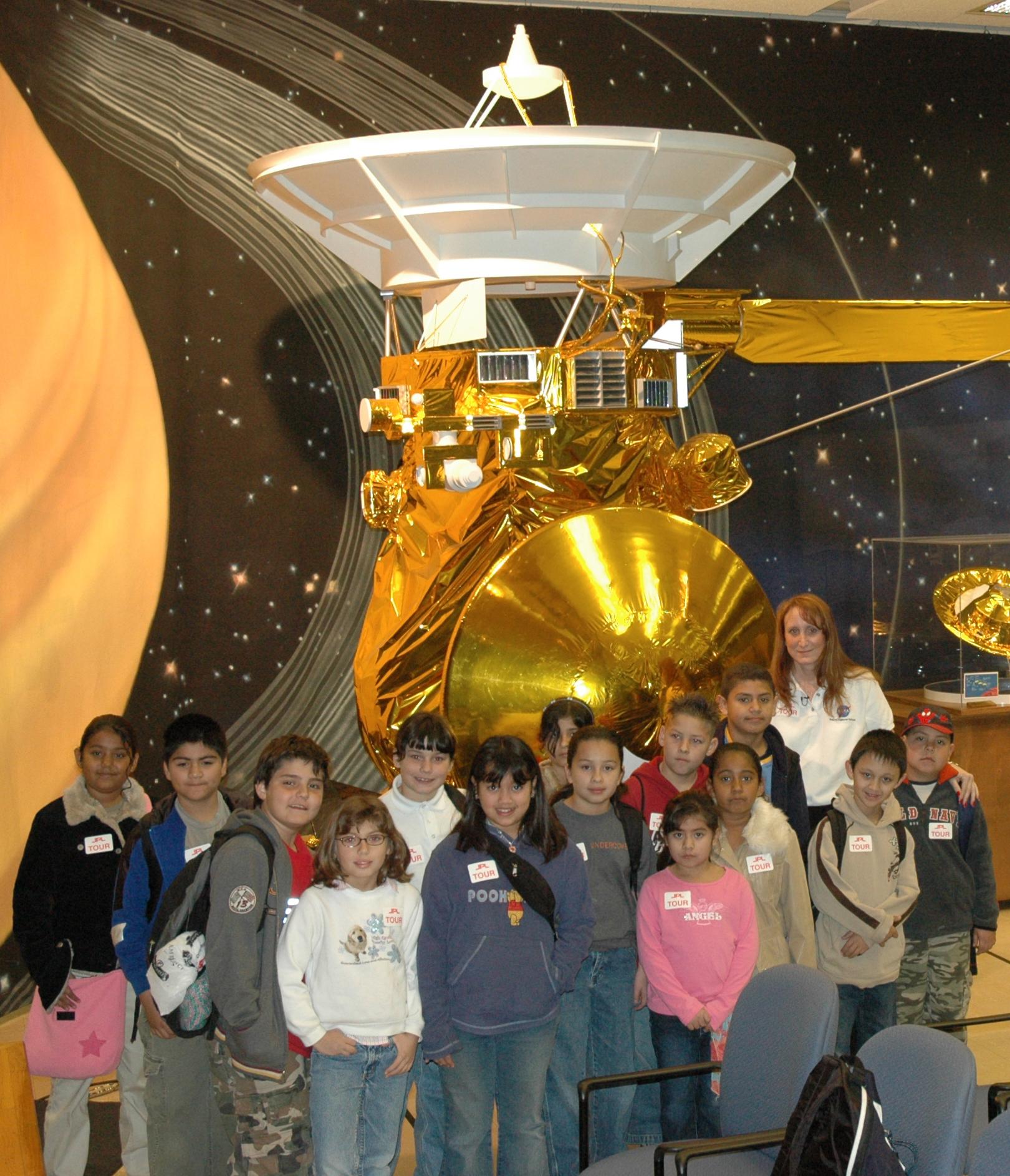 Students and their teacher pose in front of a half-scale model of Cassini