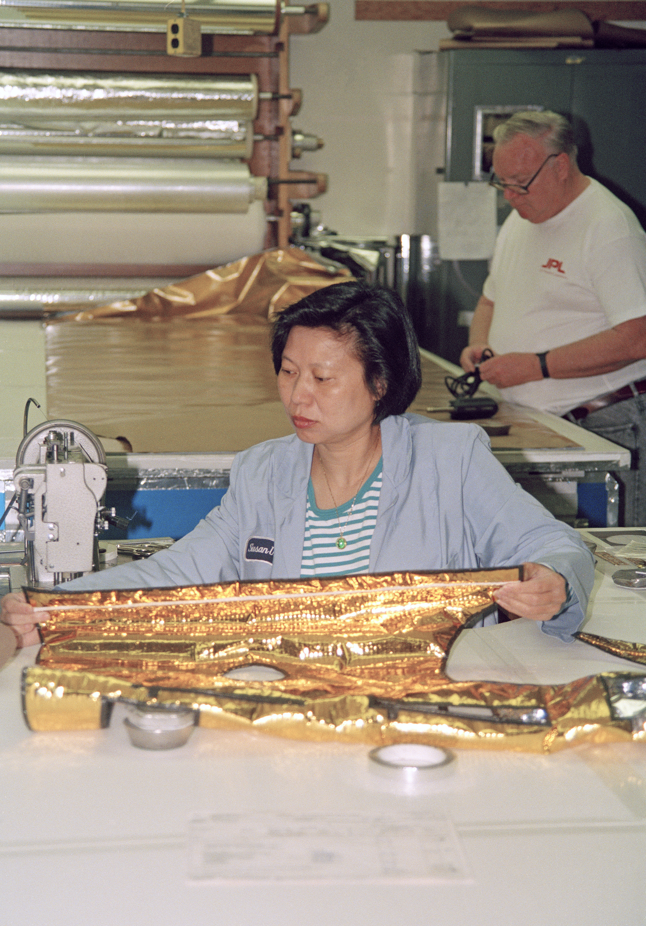 Color image of woman sewing a gold-colored thermal spacecraft blanket.