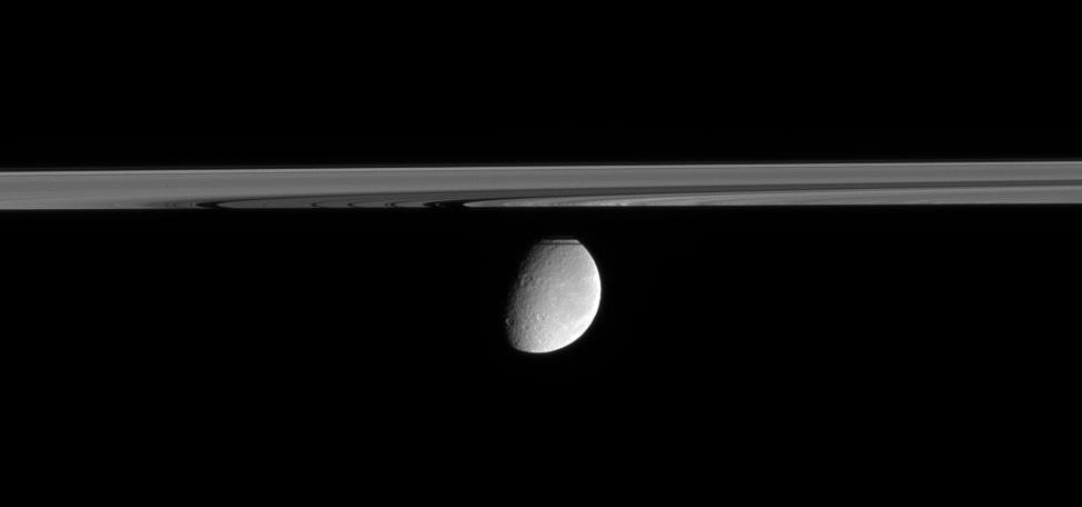Rhea floats in the distance, peeking out from behind Saturn's partly shadowed rings