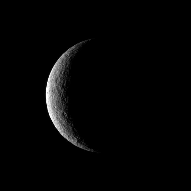 The Cassini spacecraft captures a crescent of crater-covered surface on the moon Rhea.