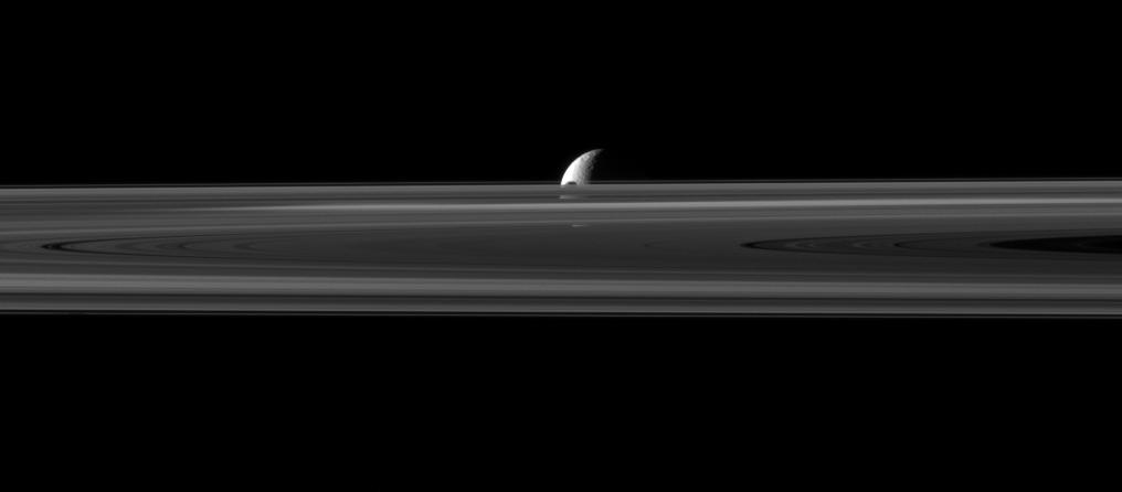 The small moon Janus is almost hidden between the planet's rings and the larger moon Rhea.