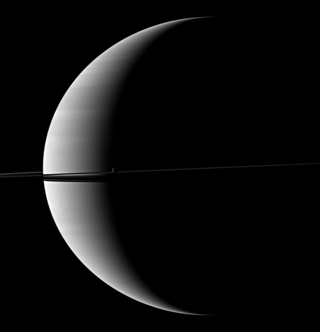 Saturn's rings and its moon Rhea are imaged before a crescent of the planet.
