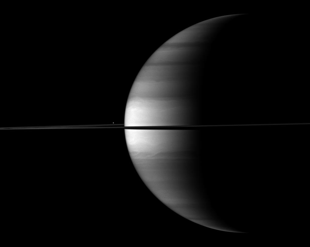 Enceladus appears as a bright dot  beyond a crescent Saturn
