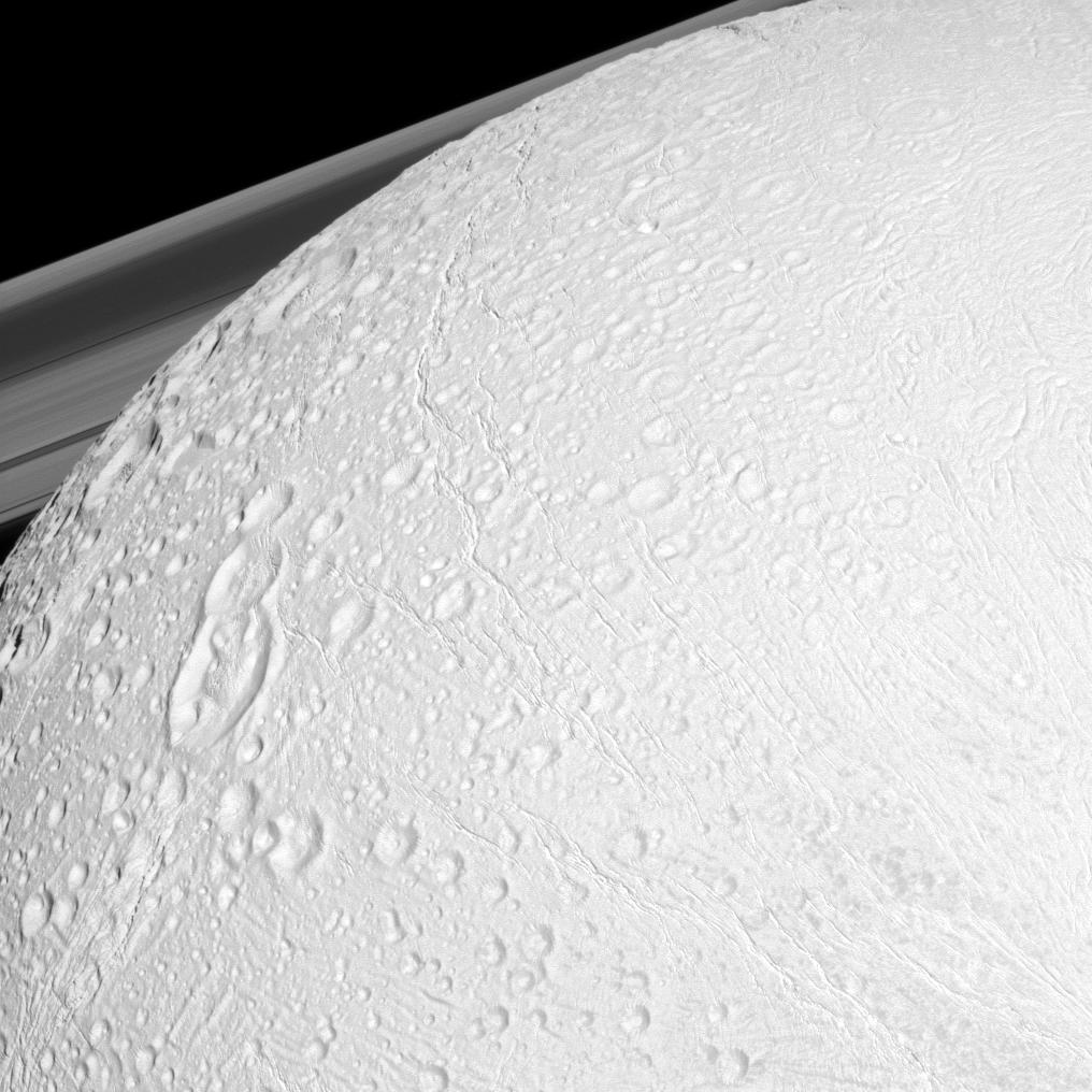 The Cassini spacecraft watches over the northern latitudes of Saturn's geologically active moon Enceladus while the planet's rings peek through in the distance in this snapshot.