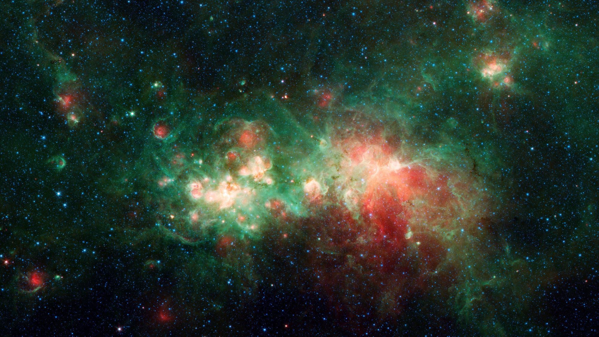 The nebula appears in shades of green, red, and yellow on a black starry background. The green swirls across the entire image with a large knot of red just to the right of center. Embedded in the green swirls are a few bright white and deep red spots that look like bubbles within the green clouds.