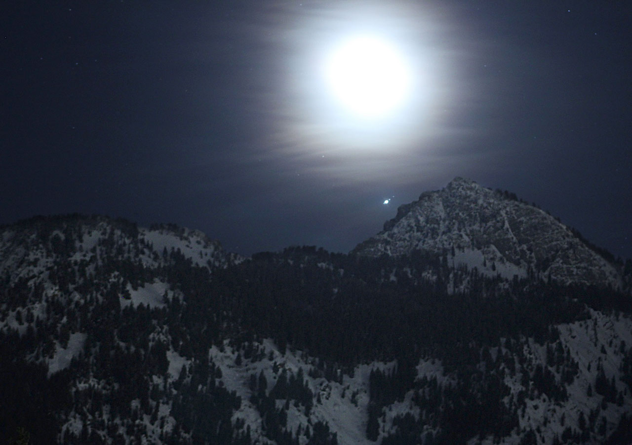 The Moon, Jupiter and its four largest moons above snowy mountain peaks in Utah.