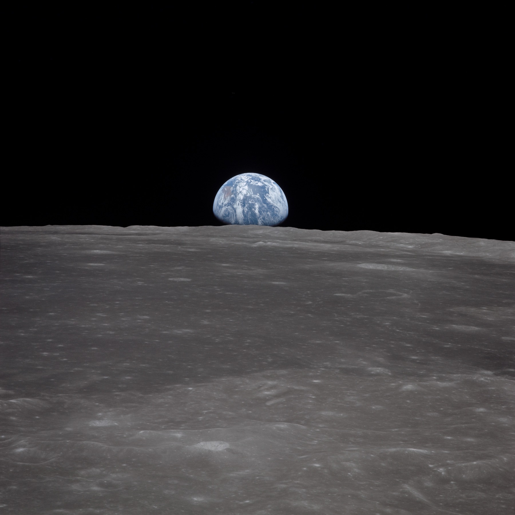 blue, gibbous phase earth rising over barren lunar surface