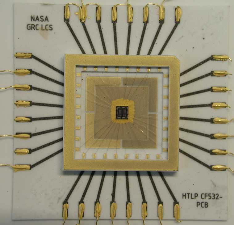 White square outlined in gold with a gold square in the middle; eight black wires with gold tips protrude from each side of the square.