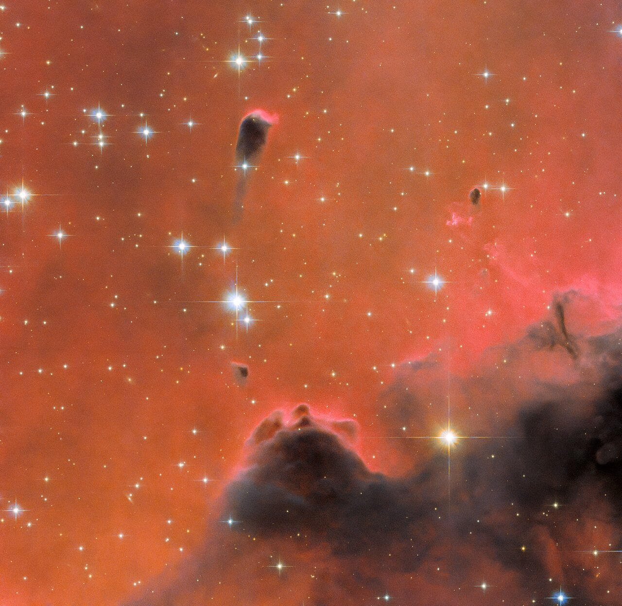 The background is filled with bright orange-red clouds of varying density. Towards the top-left, several large, pale blue stars with prominent cross-shaped spikes are scattered. A small, tadpole-shaped dark patch floats near one of these stars. More of the same dark, dense gas fills the lower-right, resembling black smoke. A bright yellow star and a smaller blue star shine in front of this.