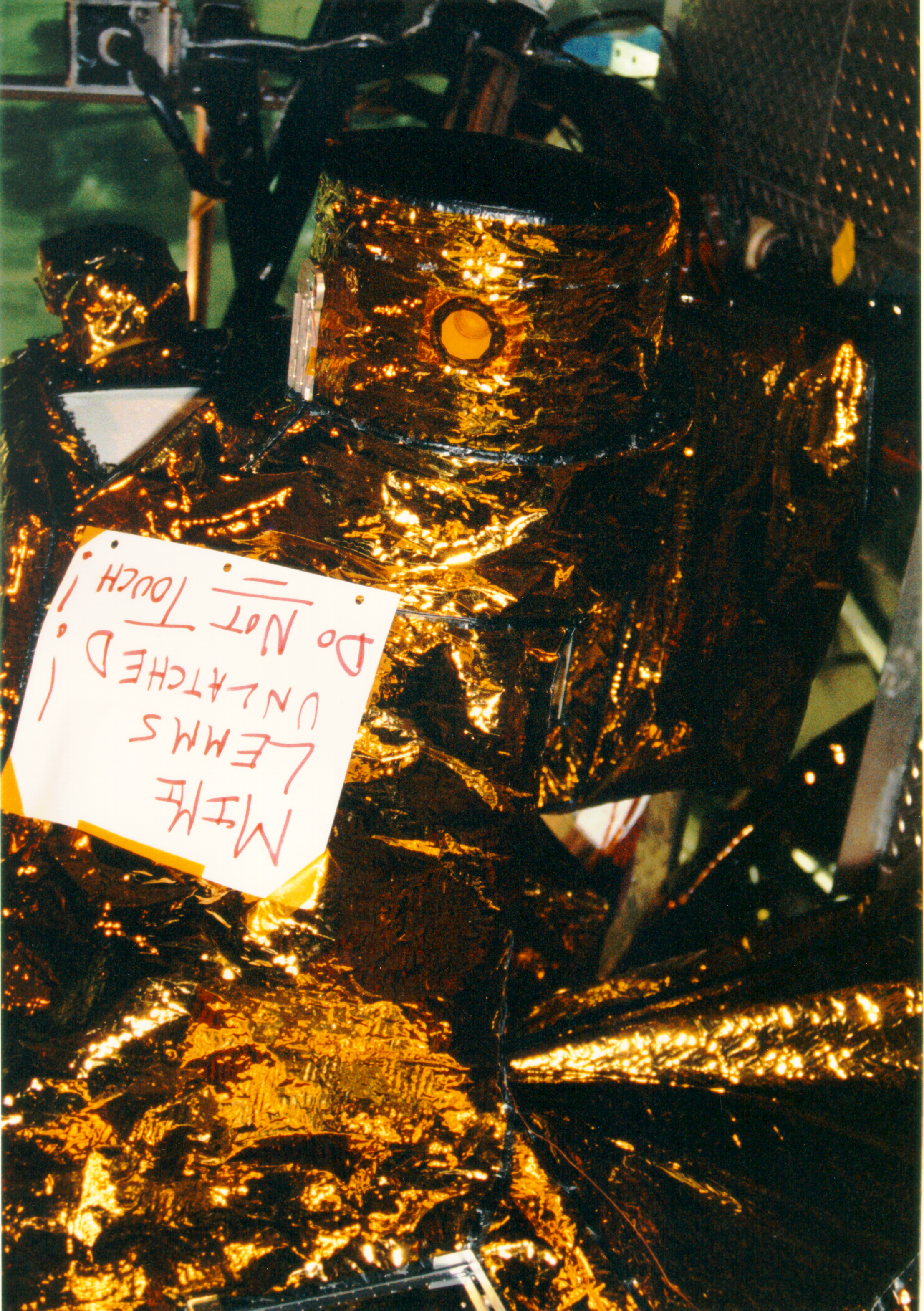 Color image of spacecraft with a note on it that says "MIMI LEMMS unlatched! Do not touch!"
