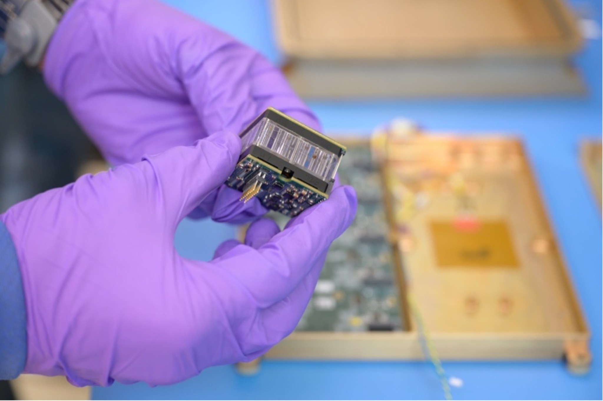 Closeup of gloved hands holding a cuboid-shaped device.