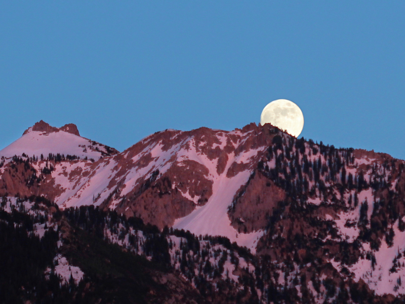 full moon over mountain ridge in pink sunset light