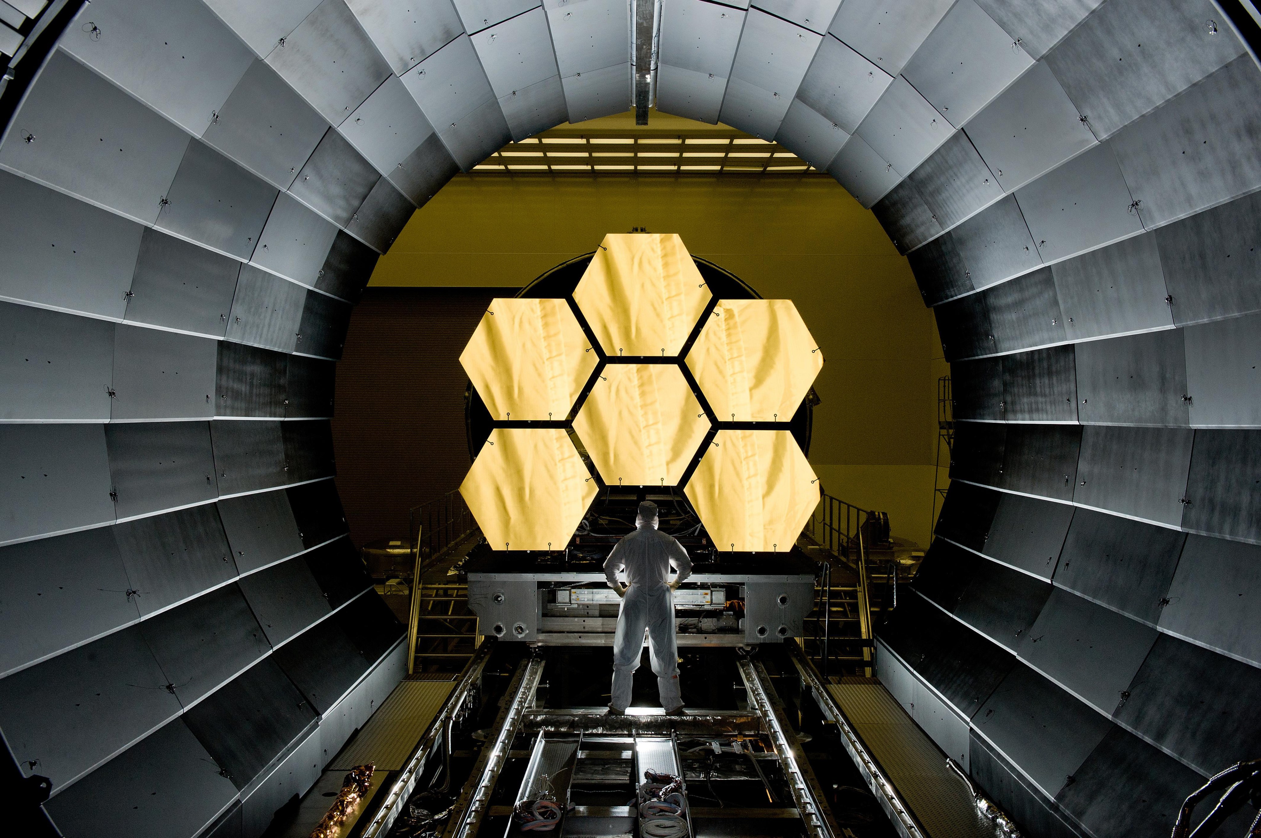 An engineer stands in front of the gold-coated primary mirror EDU