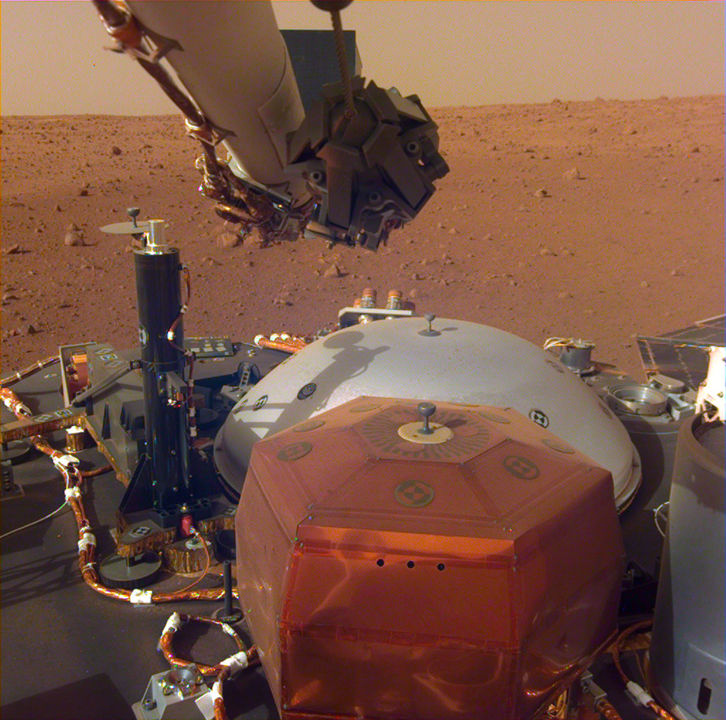 Spacecraft instruments and a view of a dusty red Martian plain.