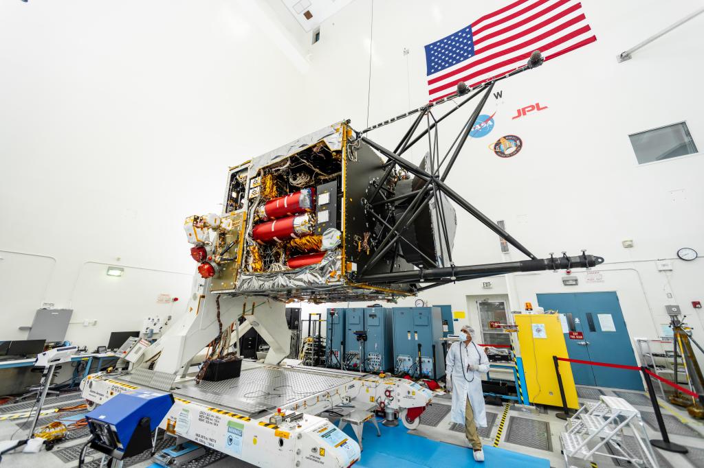 A worker stands near the Psyche spacecraft which is elevated on a work platform.