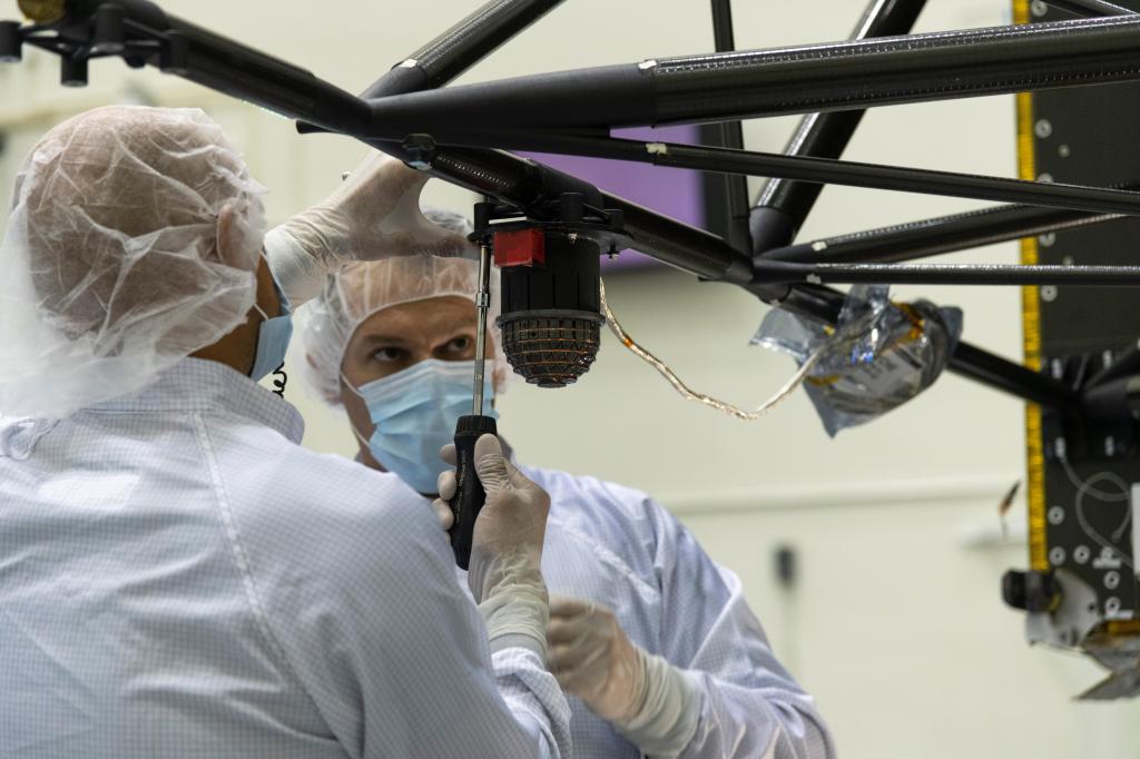 Two engineers in protective white clothing work on Psyche's magnetometer.