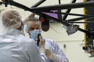 Two engineers in protective white clothing work on Psyche's magnetometer.
