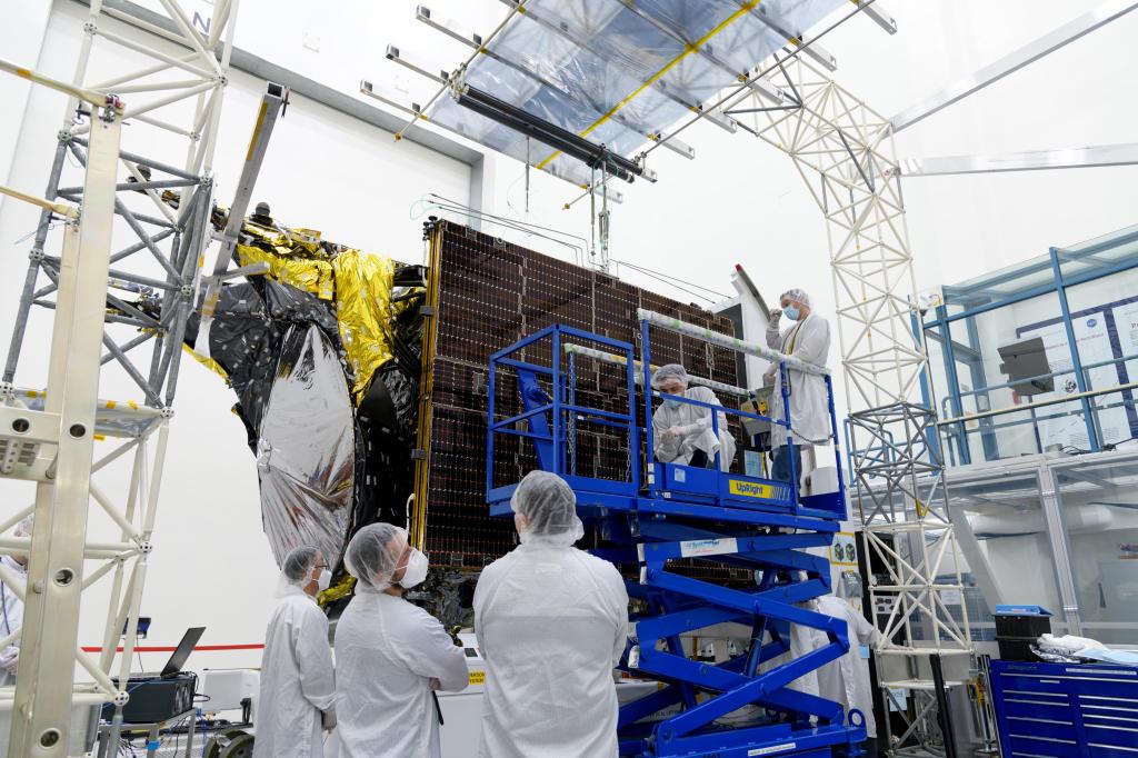 Engineers standing on the ground watch as other workers on a blue lift work on an unfurled solar array