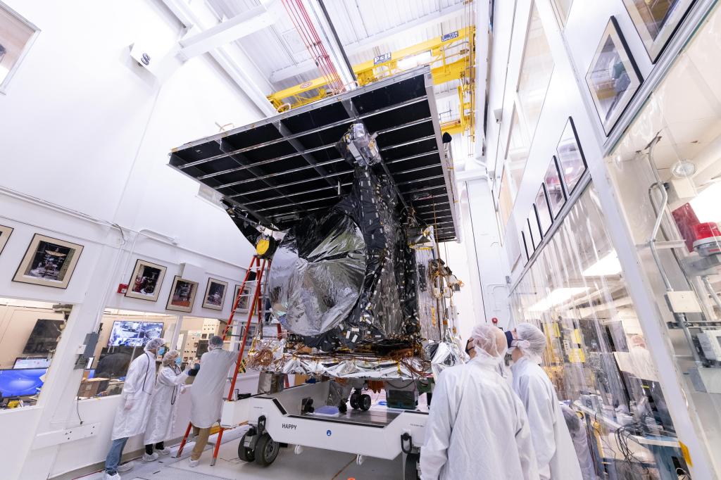 Workers watch as the Psyche spacecraft with a solar panel on top is wheeled down a hallway