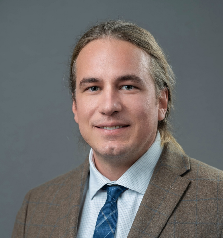 Portrait photo of a person with hair pulled-back hair wearing a blazer and a tie and a collared shirt.