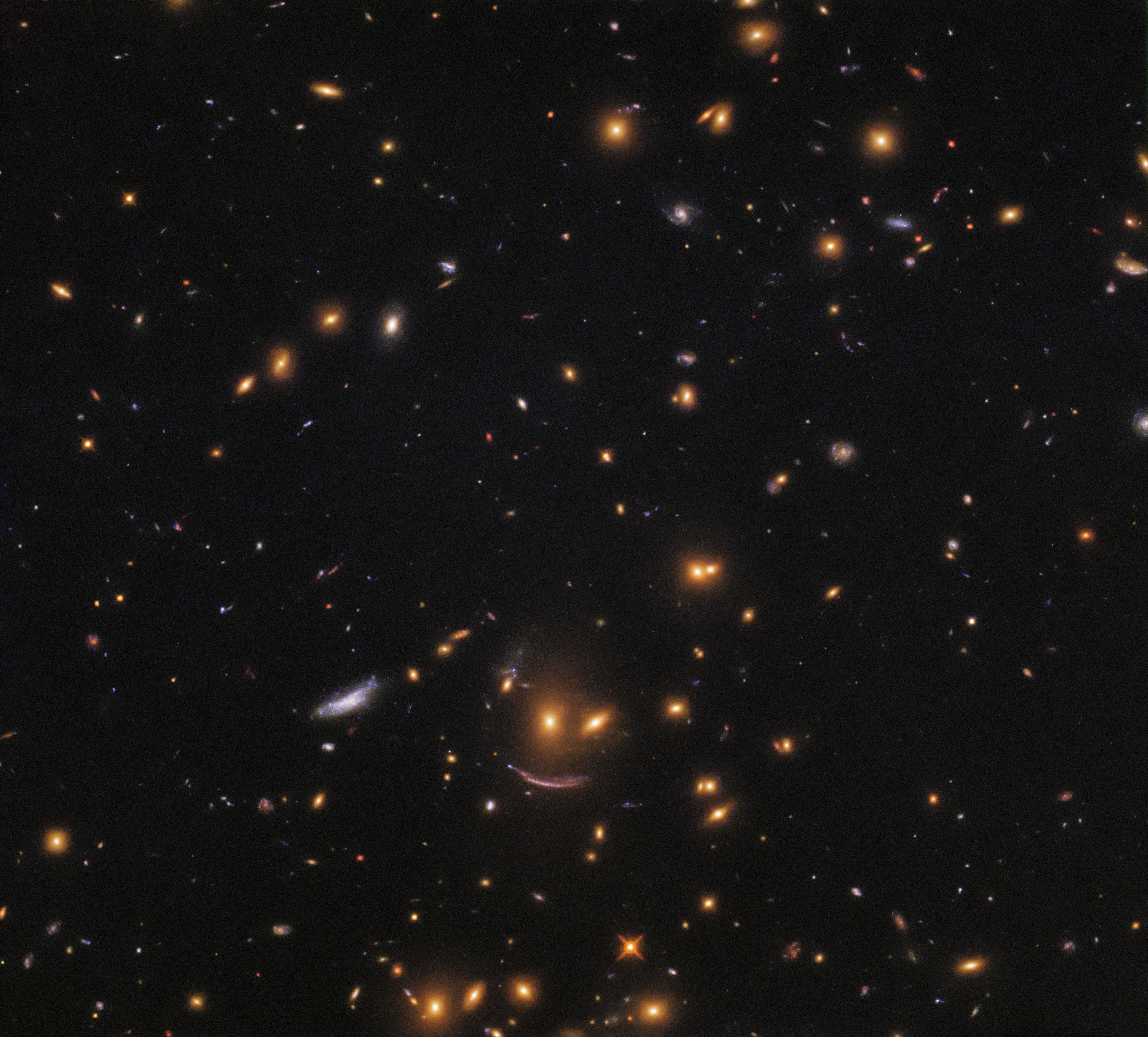 Collection of galaxies including a trio that form in the shape of a classic cartoon smiley face-- two dots for eyes and a curved line for a mouth.