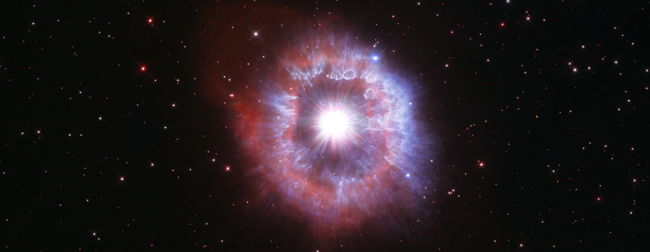 Bright-white star surrounded by a pinkish and white shell of gas. Black background dotted with stars.