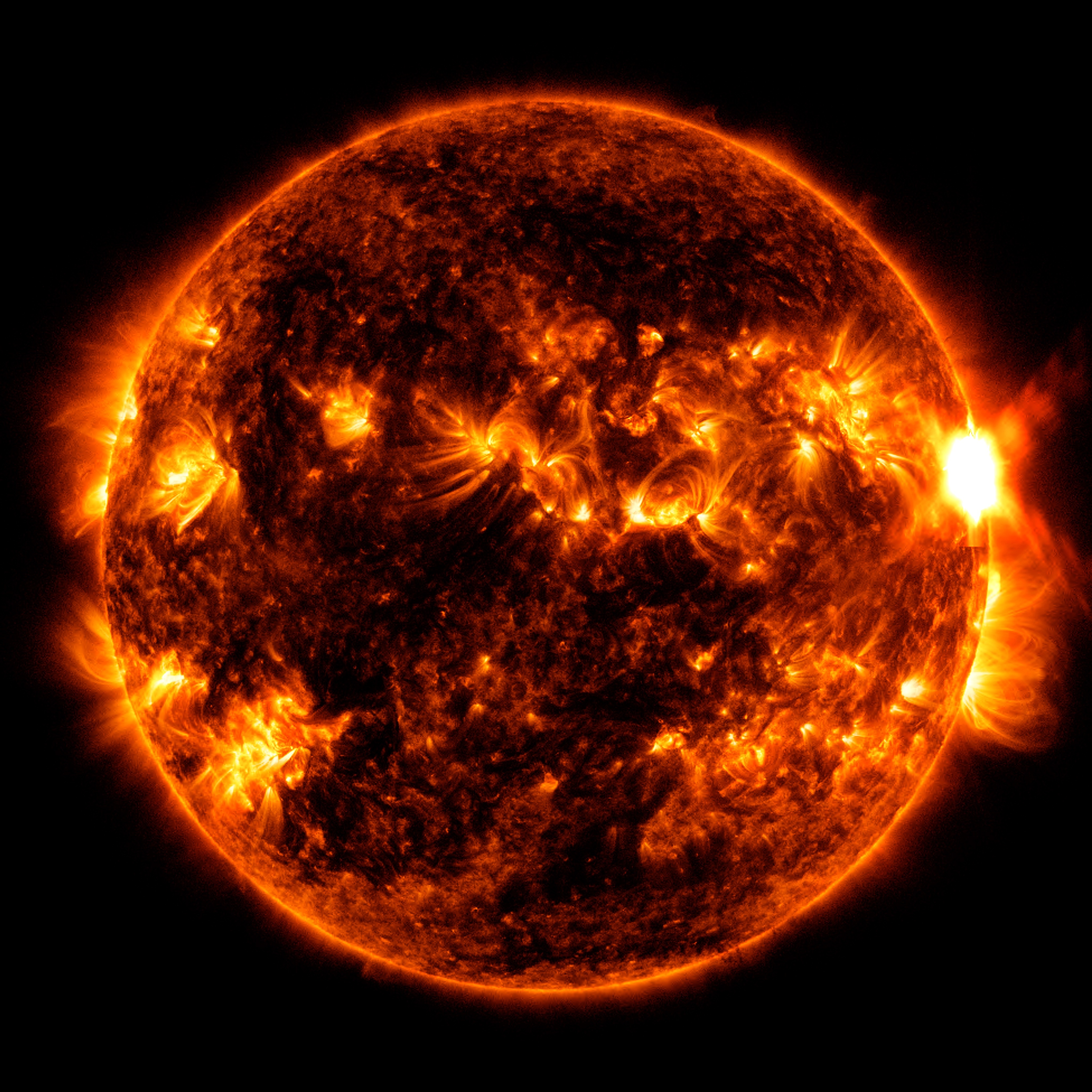 The Sun shown in red and orange, swirled with darker inactive areas and brighter active areas. On the right side of the Sun, there is a very bright region where the flare erupts.