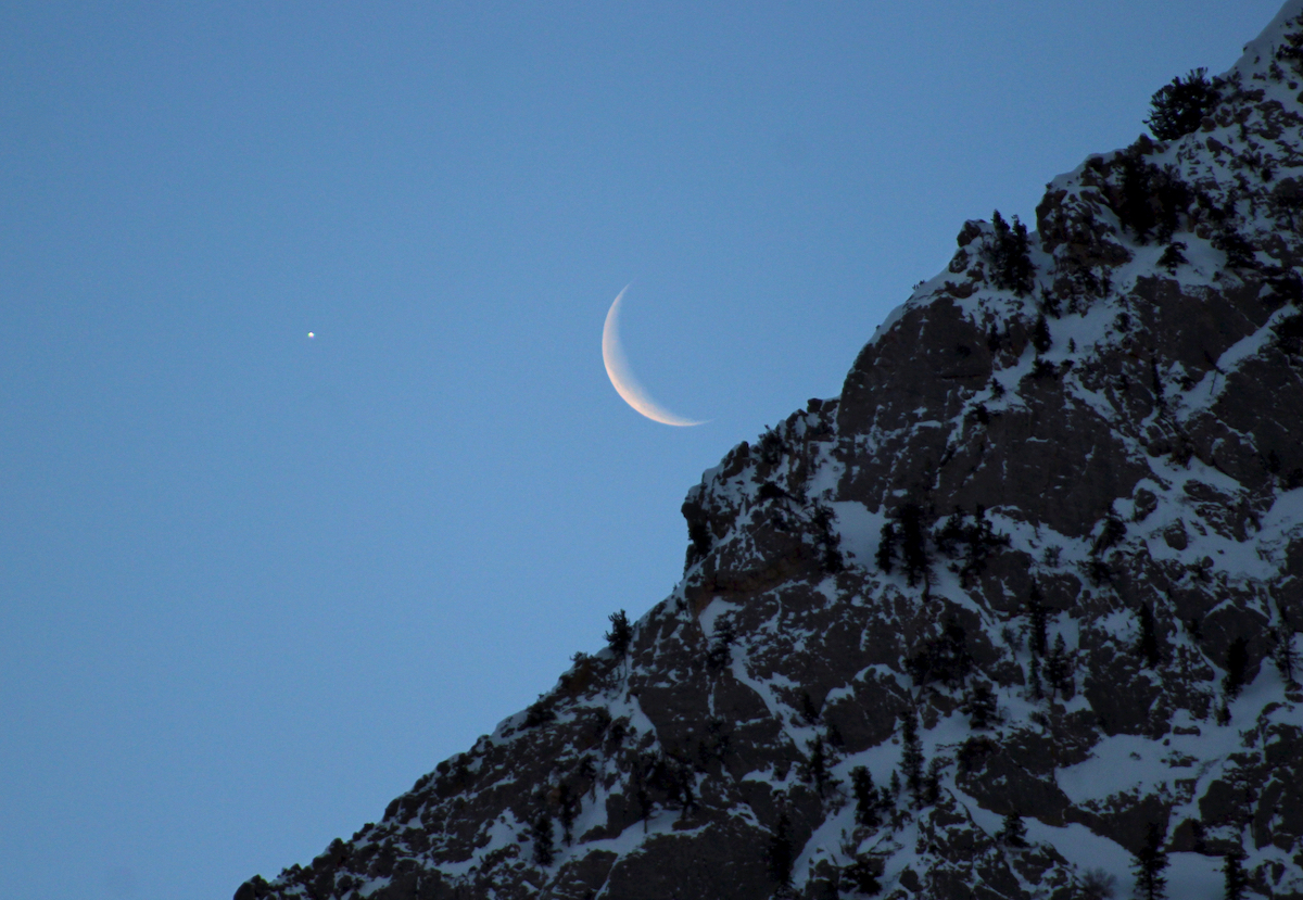 bright star and crescent moon above a rocky cliff