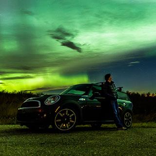 silhouette of a person and a car against a green aurora lit sky