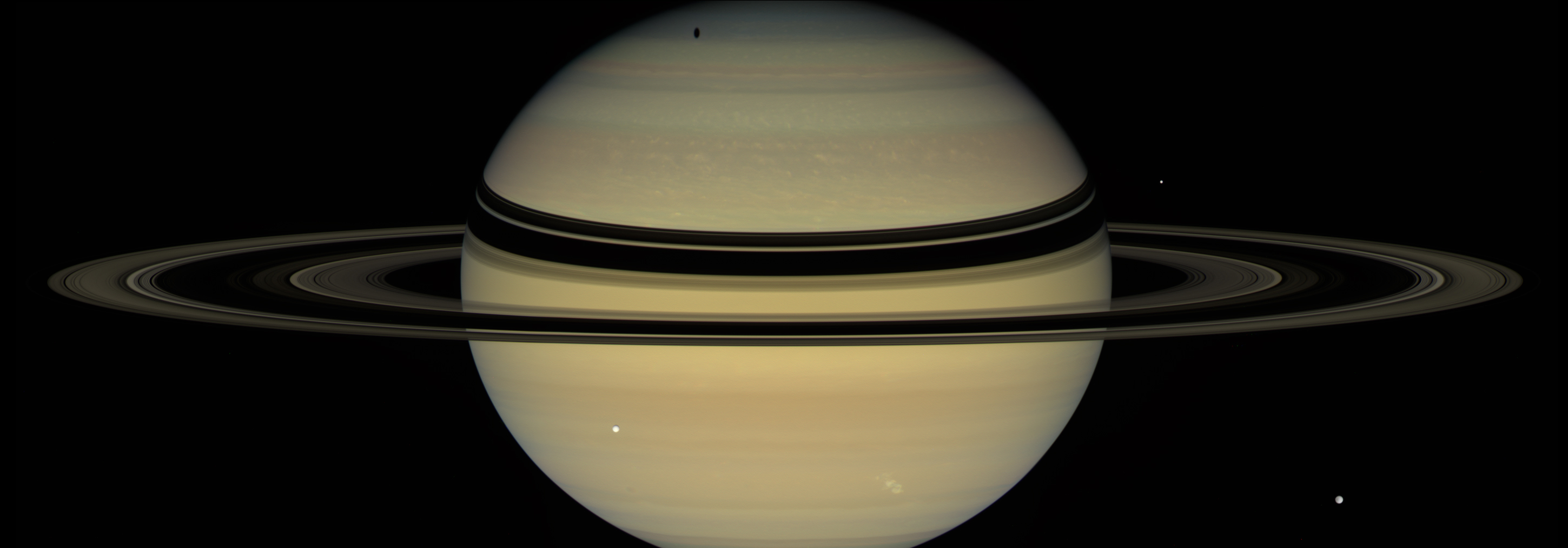 wide view of saturn and its rings with relatively smaller moons visible