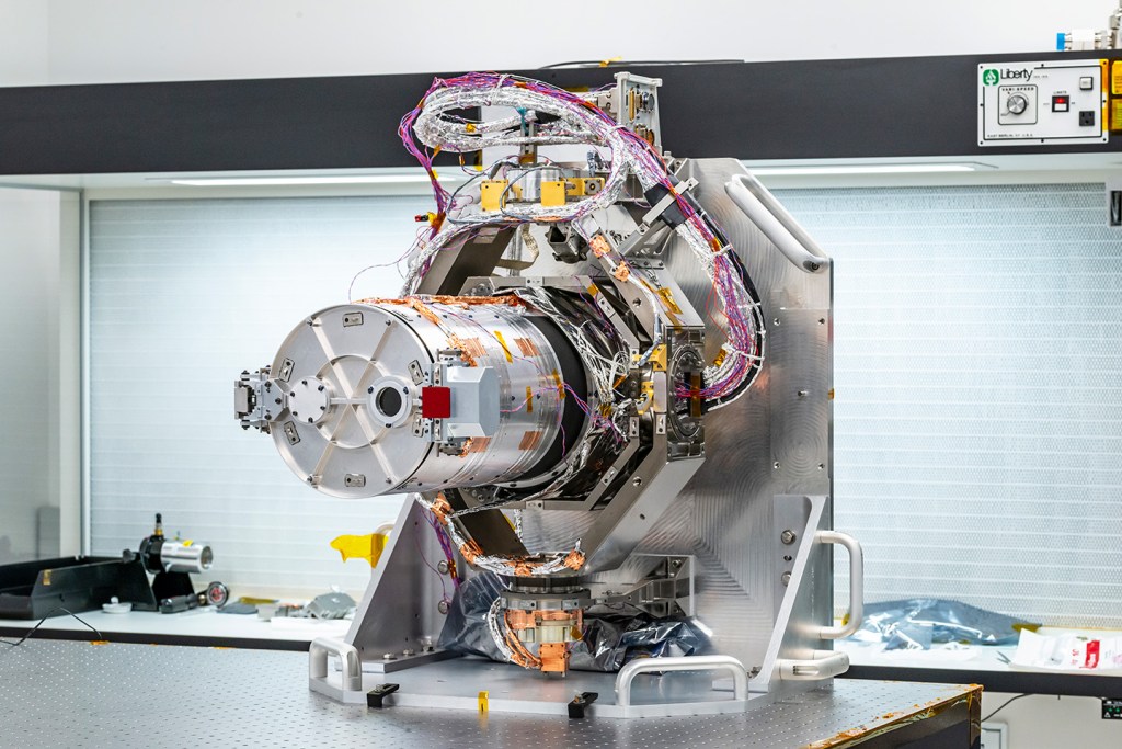 The silver-colored Europa Clipper narrow-angle camera sits on a table. Wires of various colors, including red, purple, white, and black surround the camera.