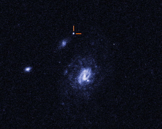 This Hubble photograph shows three galaxies against the velvet-black backdrop of space. The largest is the white and blue spiral-shaped galaxy at image center. Two smaller galaxies are whitish patches toward the left. A curious white spot near the top of the image is the brilliant glow from some unknown object that exploded, but is not associated with any of the galaxies.