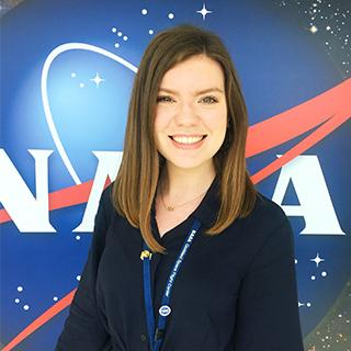 Portrait photo of a woman with long dark hair standing in front of the NASA logo